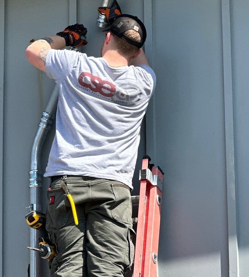 Electrician from Current Solutions Electric working on electrical installation, using tools on a ladder, showcasing expertise in Kansas City electrical services.