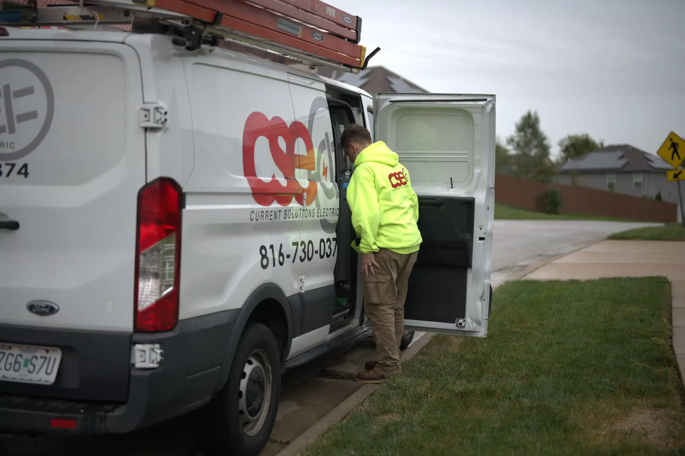 Emergency electrician in bright yellow jacket accessing Current Solutions Electric service van on Kansas City street.
