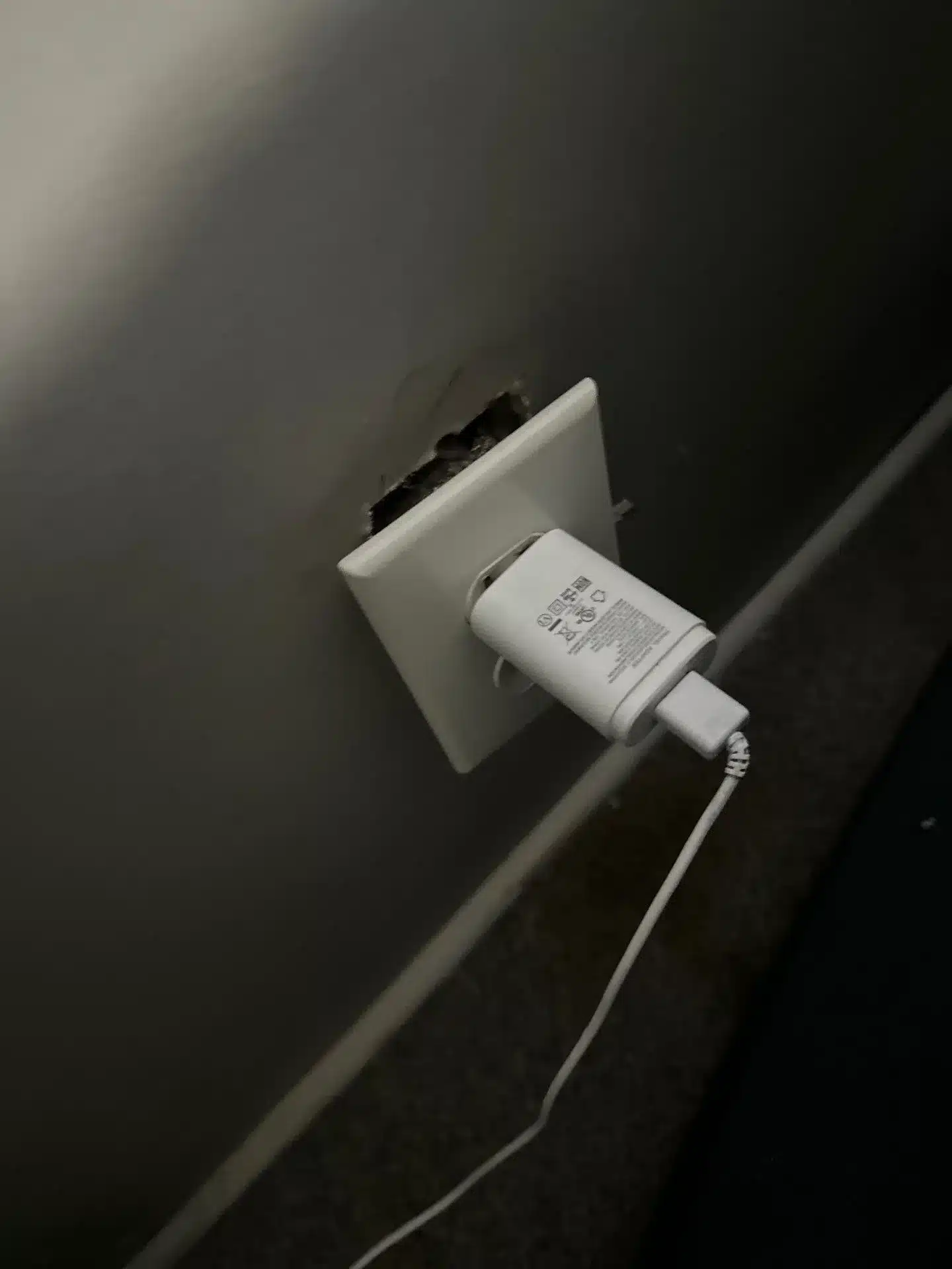 Damaged electrical outlet with charger plugged in, highlighting potential emergency electrical issues in Kansas City homes.