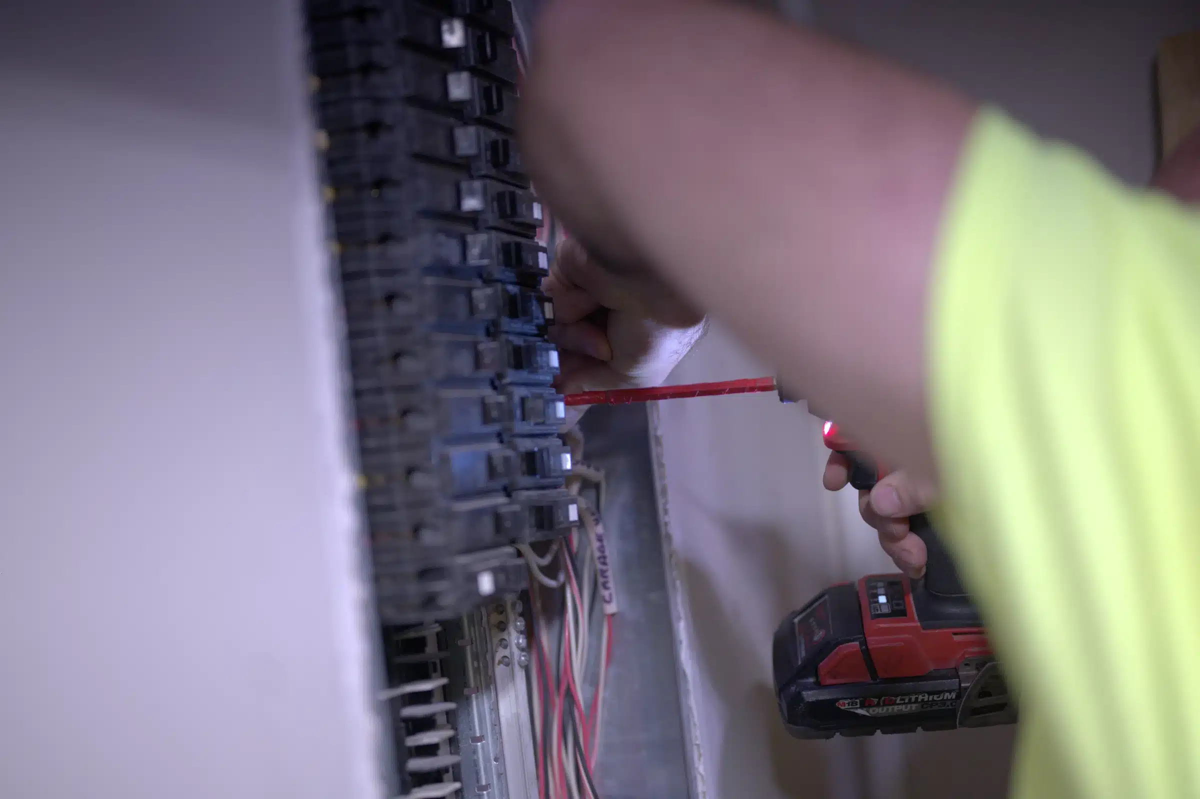 Electrician working on a circuit breaker panel, using a screwdriver and a power tool for electrical installation in Kansas City.