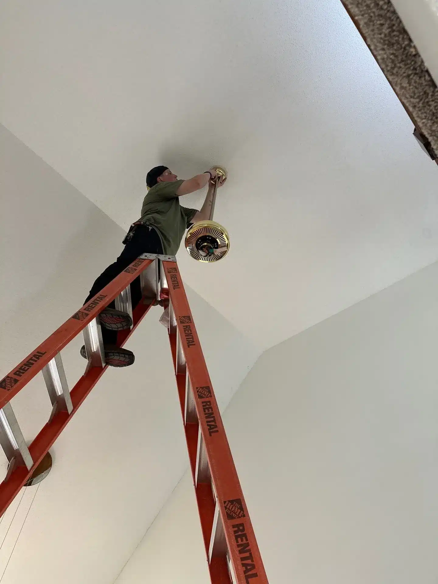 Professional electrician installing a ceiling fan on a high ceiling using a ladder, emphasizing expert ceiling fan installation in Kansas City, MO.