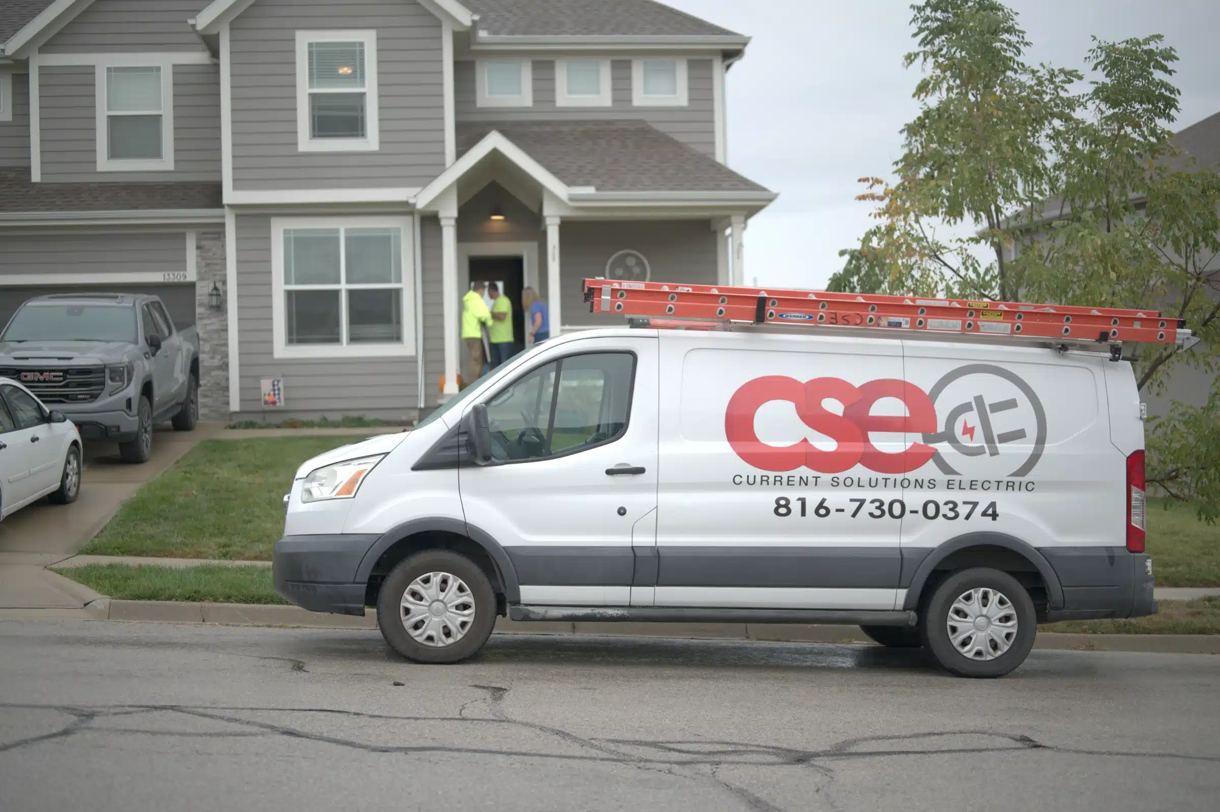 Current Solutions Electric service van parked outside a Kansas City home, featuring a ladder on top and visible contact information, with electricians at the entrance ready to assist with electrical repairs.